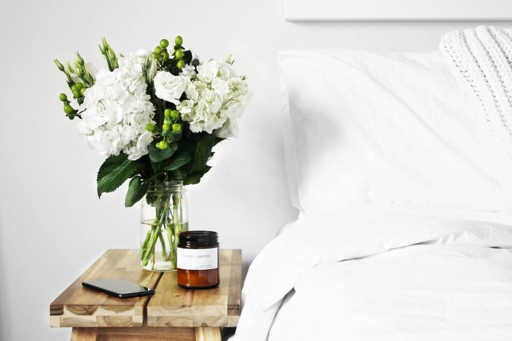 Świeca perfumowana i bukiet kwiatów na stoliku obok łóżka